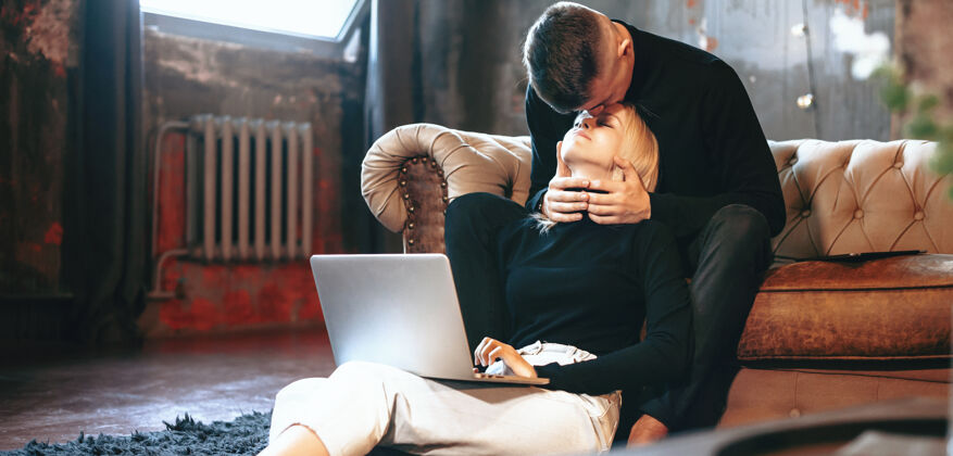 小企业一个金发白种女人拿着电脑在地板上工作 而她的爱人却在亲吻她丈夫家庭房间
