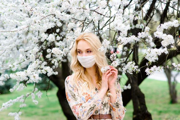 污染在春天的花园里 一个戴着无菌医用防护口罩的年轻女子花朵防护流感
