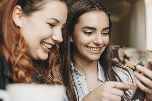 吃两个可爱的年轻女朋友坐在咖啡馆里看着一部t智能手机微笑着玩得很开心木头甜点美味