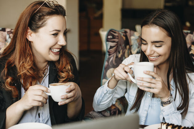 影响者迷人的大号红发女人喝着咖啡 微笑着和她可爱的女朋友在咖啡馆里餐厅友谊互联网