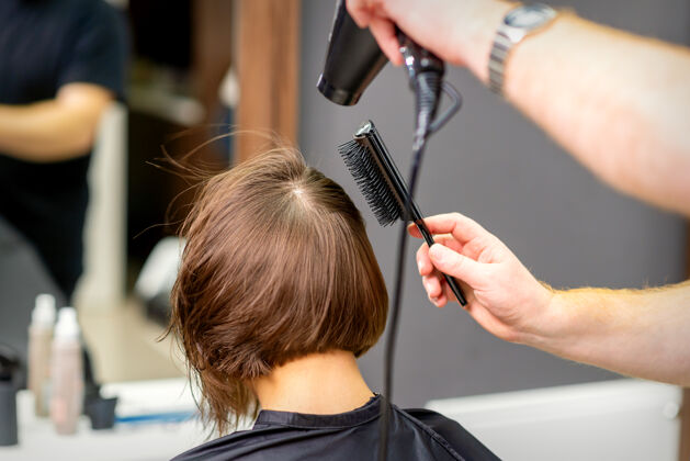 理发师美发师在美容院里把年轻女子的棕色头发吹干设备成人年轻人