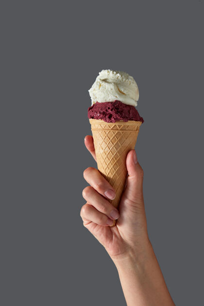 冷藏一只雌性的手拿着红莓冰淇淋和白牛奶冰淇淋 放在灰色的桌子上的华夫饼筒里墙.夏季复制空间概念奶油华夫饼球