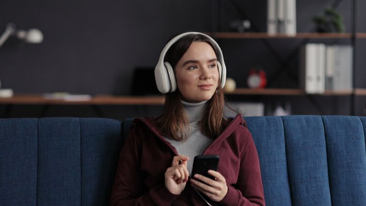 女人戴着耳机微笑的年轻女孩的肖像 在移动应用程序中选择喜爱的音乐曲目室内女人女孩