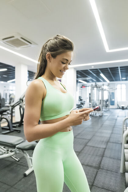 后视图在健身房使用智能手机的黑发女人的侧视图长凳肌肉身体