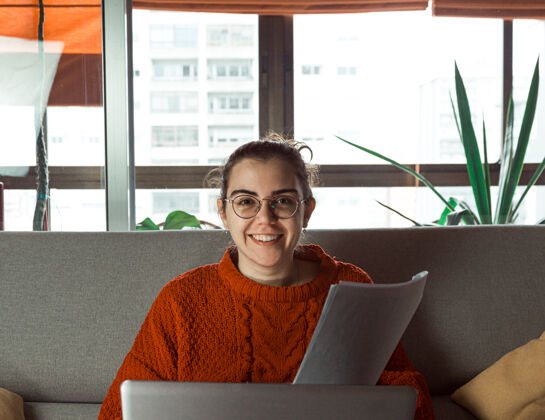 文件一个戴眼镜的年轻女子在家里的沙发上对着他的笔记本电脑微笑女性放松长发