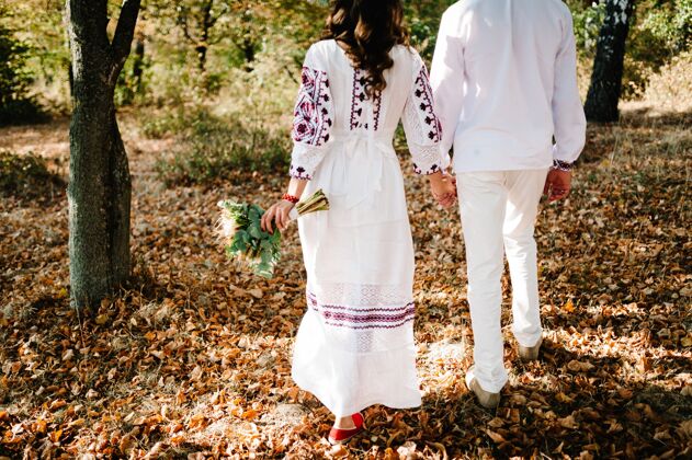 女性新婚夫妇在秋天去看风景乌克兰公园风格：女人 男人穿绣花衣服 带着花束走在路上自然 民族穿着民族服装参加婚礼服装人秋天