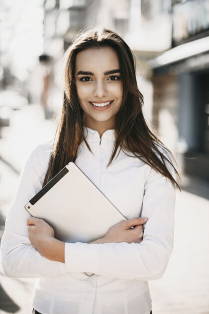 自信一位可爱的年轻女商人的肖像 她留着一头乌黑的长发 面带微笑地看着相机 手里拿着一块平板电脑走在街上黑发使用衬衫