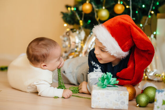 小一个小男孩和他的弟弟在圣诞树下玩礼物乐趣男孩家庭