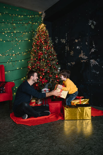 男孩年轻漂亮的父亲带着可爱的儿子在圣诞树旁礼物快乐圣诞节漂亮女孩阁楼