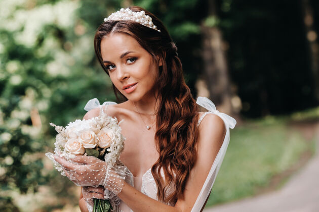 手套一个优雅的新娘在一个自然公园里穿着白色的裙子和一束花束的肖像公园水模型