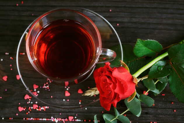 玫瑰茶放在透明的杯子里 彩色的糖果和一朵红玫瑰放在暗处健康热形状
