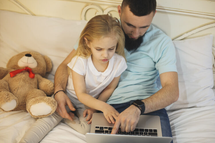 童年上图是一个可爱的小孩看着笔记本电脑的屏幕 她的父亲在家 靠在床上早上好 爸爸还有女儿在看电影玩具在线教学