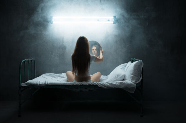 女孩疯女人带着镜子坐在床上 失眠 黑暗的房间…迷幻的女人每晚都有问题 抑郁和压力 悲伤 精神病院恐怖精神病问题