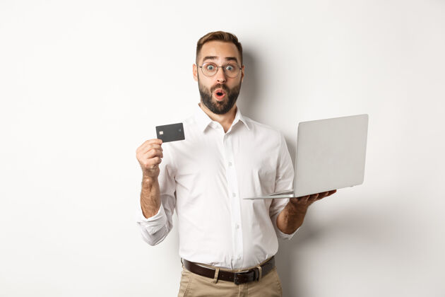 男在线购物惊讶男人拿着笔记本电脑和信用卡 在网上商店购物 站在白色背景上房地产经纪人BusinessFinance