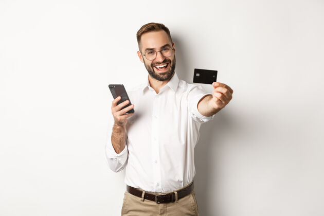 Application商务和在线付款兴奋一个拿着智能手机拿着信用卡的男人 满意地站在白色背景下BusinessManLogoManager