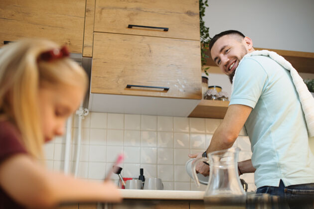 灰尘年轻的留着胡须的父亲一边洗碗 一边微笑着看着母亲工作时正在厨房里画画的父亲男人室内爸爸
