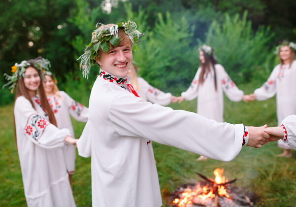 花仲夏年轻穿着斯拉夫人衣服的人在盛夏围着火转美丽交谈仪式