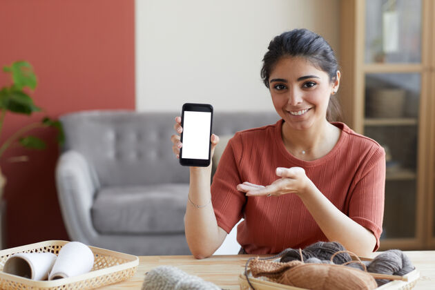 舒适照片中的年轻女子面带微笑 指着手机 她在工作中使用在线程序快乐肖像家庭房间