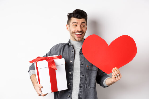 模切快乐的男朋友在情人节约会时送浪漫的礼物 手里拿着礼物盒和大大的红心卡 笑容欢快 洁白丈夫情感提议
