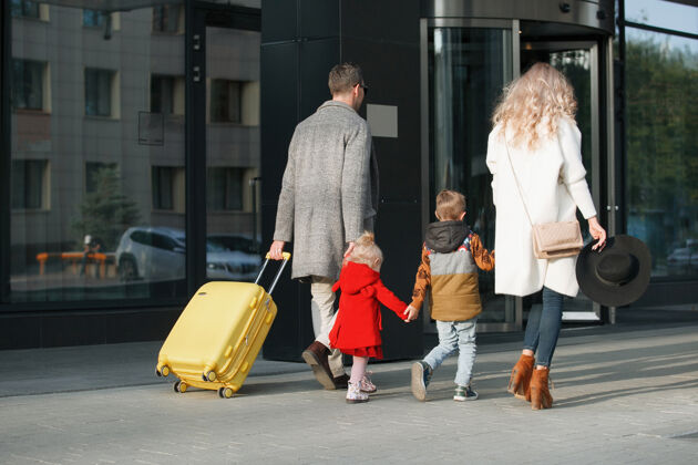包游客一家 爸爸 妈妈 女儿和儿子拿着一个黄色的手提箱进入酒店等待旅行牛仔裤