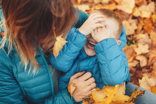 秋天俯视图中 一个可爱的小男孩靠在妈妈的腿上笑着 用手遮住脸户外玩耍活跃