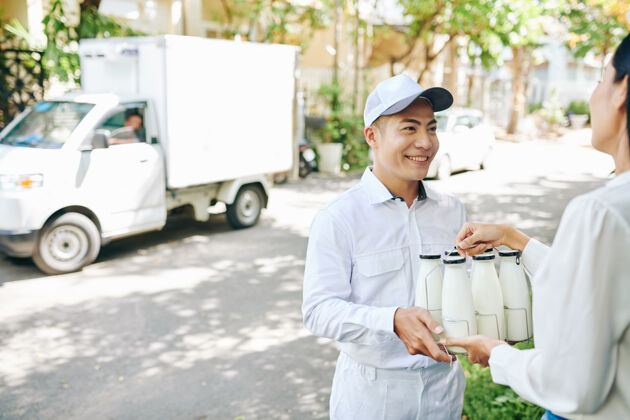 服务微笑的送奶工给漂亮的女顾客送奶瓶男性订单亚洲