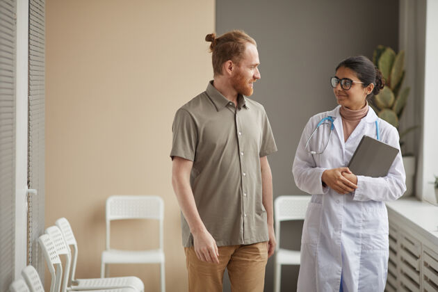 制服穿着白大褂的年轻女医生在医院走廊上与男病人交谈医生表情医务室