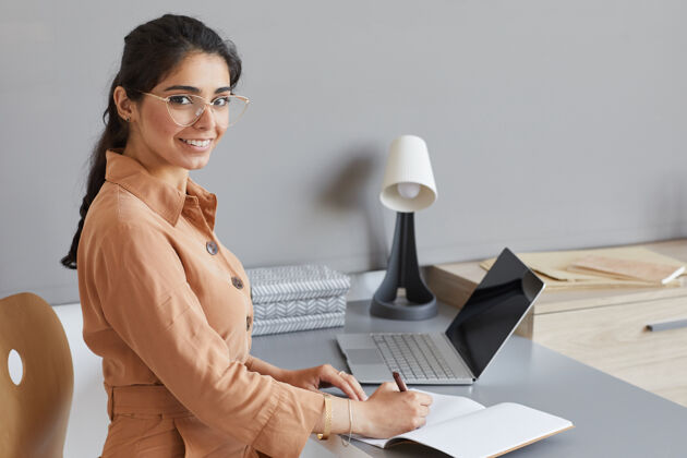 专业职业年轻女商人坐在办公室的桌子前微笑 在笔记本上写计划的画像美女办公桌无线技术