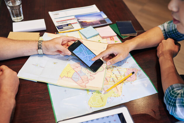 海岸年轻人计划旅行 他们正在查看纸质地图和智能手机上的在线应用程序度假合作坐
