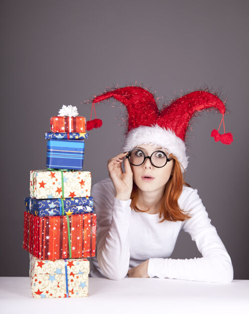 快乐滑稽的红发女孩戴着圣诞帽 戴着带礼盒的眼镜礼物服装包装