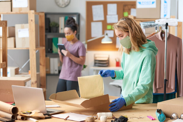 专业职业一位年轻的女士 戴着口罩 和同事站在工作间的墙边 包着一个包裹仓库微笑团队