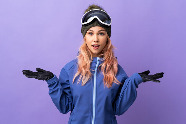 惊人带着滑雪眼镜的滑雪者女孩脸上孤立的紫色带着震惊的表情人手势震惊