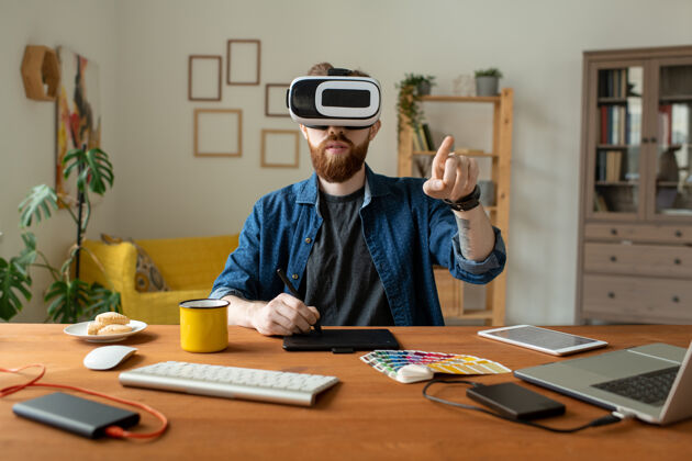 笔记本电脑严肃的大胡子设计师坐在桌子旁 在家里使用虚拟现实模拟器时 在数字化仪上画画商务职业成人