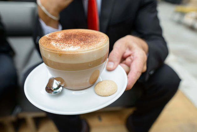 休息商人端着一杯卡布奇诺咖啡 泡沫上撒着巧克力 旁边放着饼干男人行政人员帅气