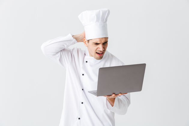 厨师面带沉思的厨师身穿制服站在白色的墙上 手里拿着笔记本电脑员工烹饪便携