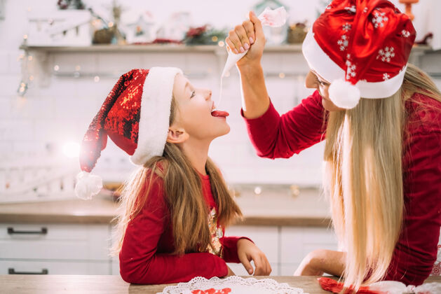 烘焙穿着围裙的妈妈和她十几岁的女儿戴着圣诞老人的帽子在厨房里玩得很开心聚会玩耍女人