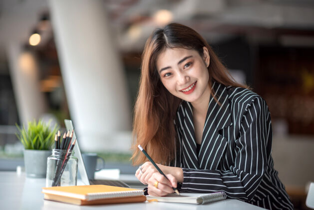 工人年轻漂亮的亚洲女商人坐在办公室里 看着镜头 开心地笑着企业家职业西装
