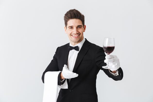 工作年轻帅气的侍者穿着燕尾服 端着一杯红酒隔着灰色的墙白种人工人男性