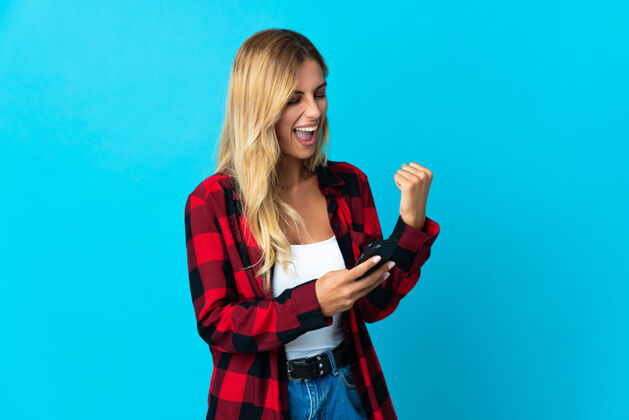 现代年轻的金发乌拉圭女人拿着手机在胜利的位置互联网年轻聪明