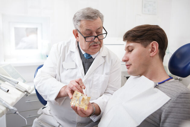 男人上了年纪的男牙医在诊所工作 和病人说话牙科牙科牙痛