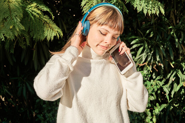 成人一个漂亮的白人女孩在公园里戴着蓝色耳机听音乐姿势女人女孩