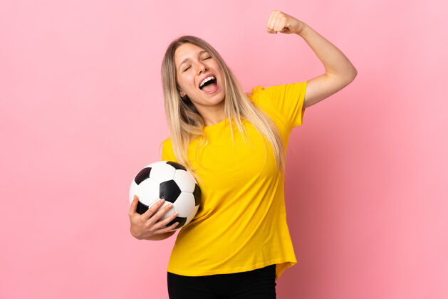 拳头一个年轻的足球运动员 一个被隔离在粉红色上庆祝胜利的女人成人运动员积极