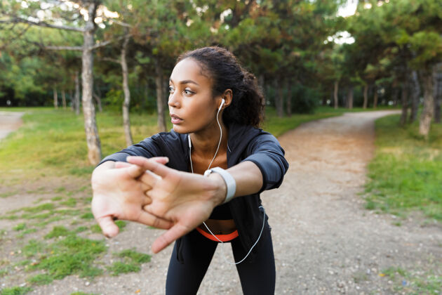 运动员一幅20多岁的美国黑人妇女穿着黑色运动服在绿色公园里锻炼身体的画像成人耳机减肥