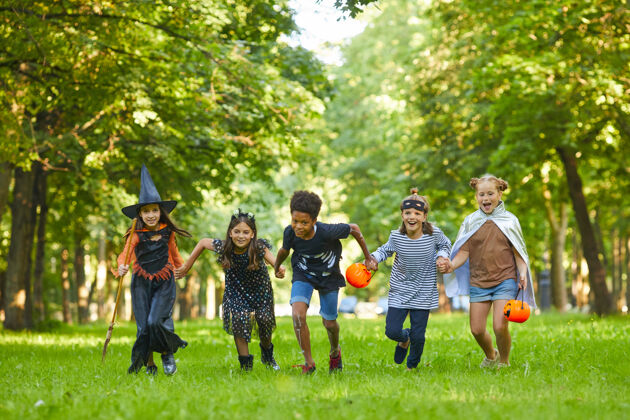 聚会社交活动一群穿着万圣节服装的孩子在公园的绿草上奔跑 他们在聚会上玩得很开心春天享受童年