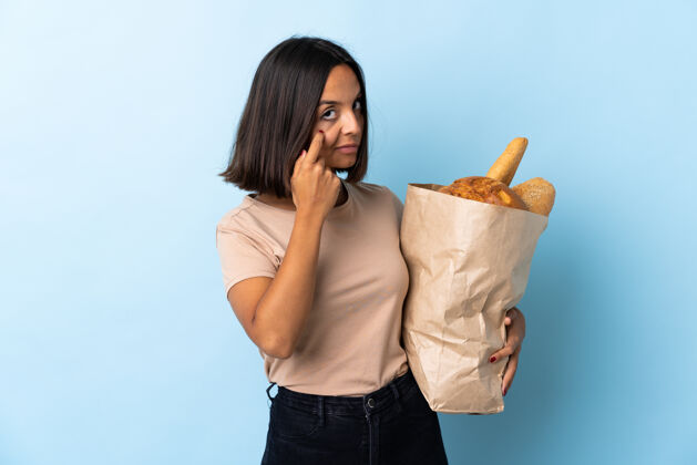 成人一个年轻的拉丁女人在买一些孤立在蓝色上的面包食物面包烹饪