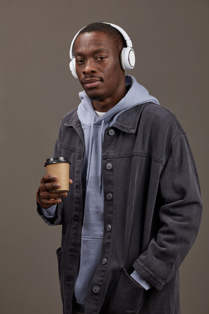 耳机身着时尚服饰的年轻人手持咖啡 欣赏音乐的写真看室内微笑