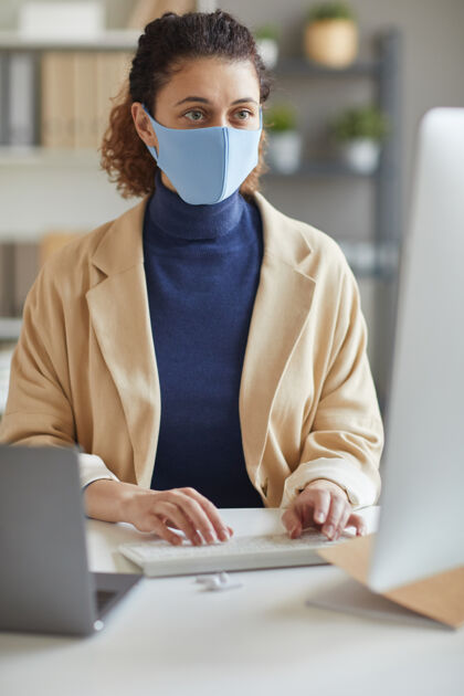 技术戴着防护面具的年轻秘书坐在办公室里用电脑键盘打字商务人士流行病注意力集中