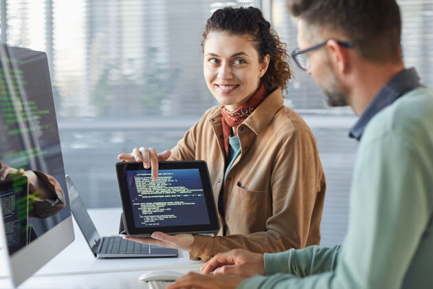 商务人士一位年轻的女士拿着数字平板电脑 向同事展示屏幕上的新软件 而他们正在团队中工作无线技术桌子专业职业