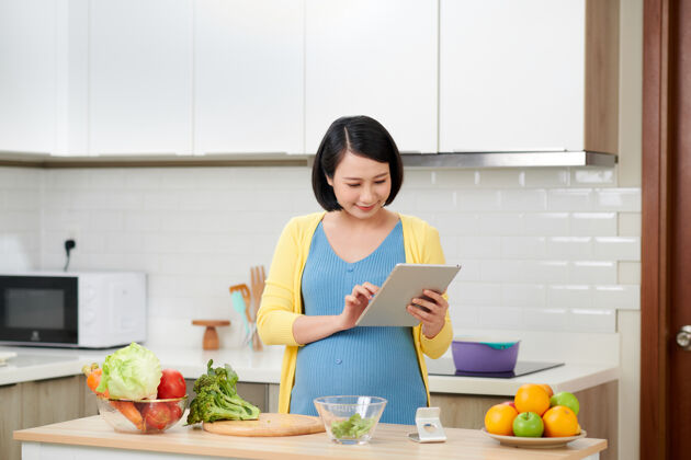 怀孕孕妇在厨房用数码平板做健康沙拉平板电脑亚洲有机