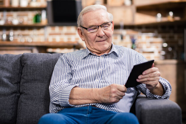 通信快乐的老人坐在沙发上看电子书人室内阅读